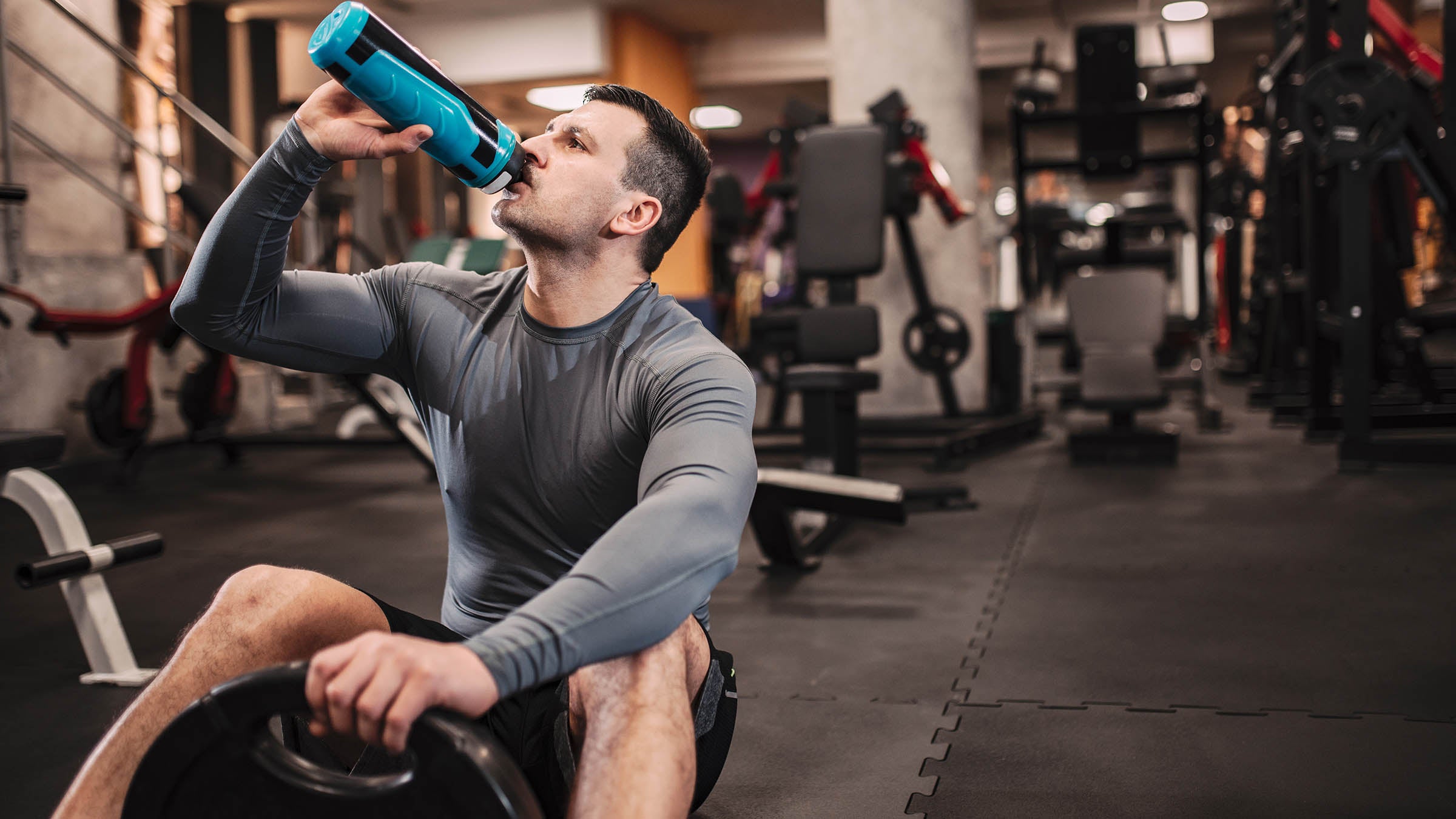 Sportsman drinking water post-workout on gym floor
